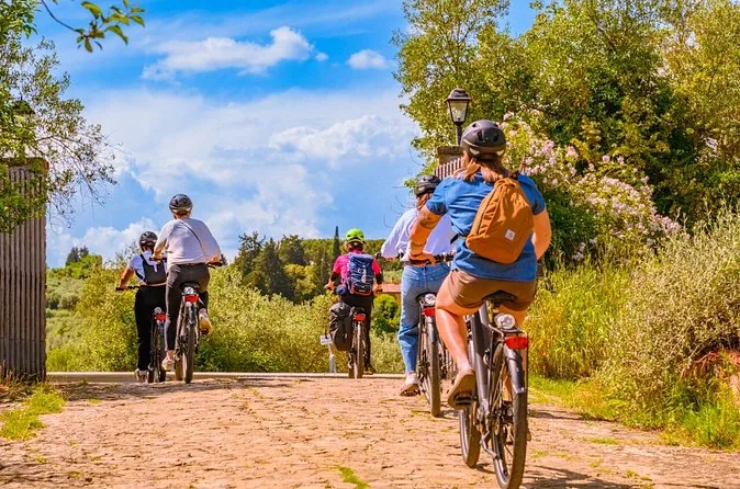 Cyclists on e-bikes riding a gravel road through trees and vineyards